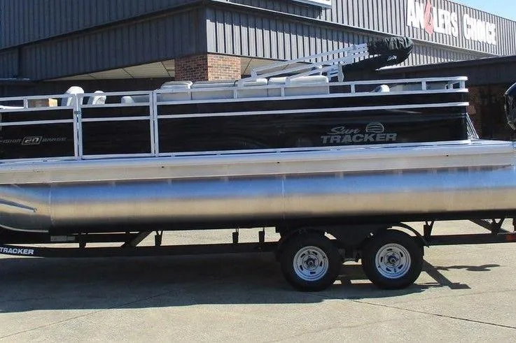 The Image of 2026 Sun Tracker Fishin' Barge 20 DLX pontoon boat on trailer outside a building. - 1