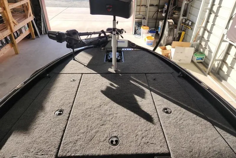 Slide: The Image of 2026 Triton 19 TrX Patriot boat interior with carpeted deck in a garage setting. - 12