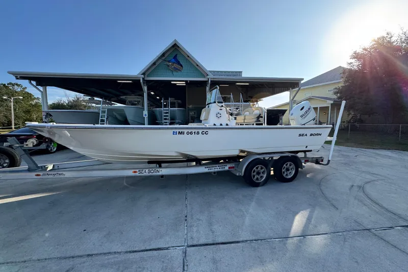 Slide: The Image of 2021 Sea Born FX24 Bay boat on trailer, parked outdoors near a building. - 2