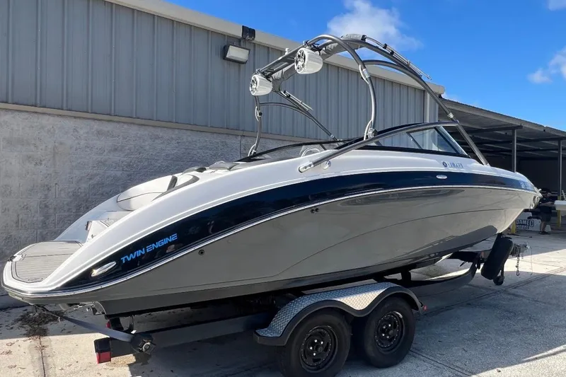 The Image of 2014 Yamaha AR240 boat on trailer, twin engine, parked outdoors. - 0