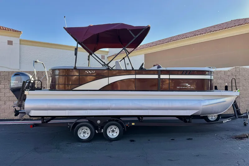 The Image of 2023 Bennington 22 XSR pontoon boat with maroon canopy on trailer, side view. - 0