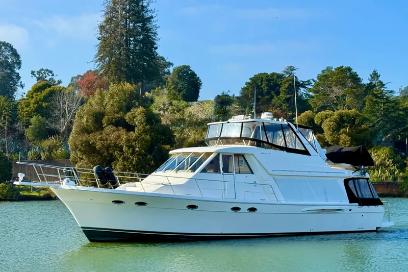 Slide: The Image of 2004 Meridian 490 Pilothouse yacht cruising on a serene lake with lush greenery. - 67