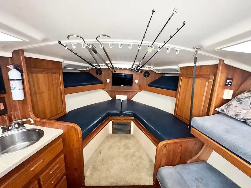 Slide: The Image of 1998 Luhrs 32 Express cabin interior with seating, fishing rods, and kitchenette. - 2