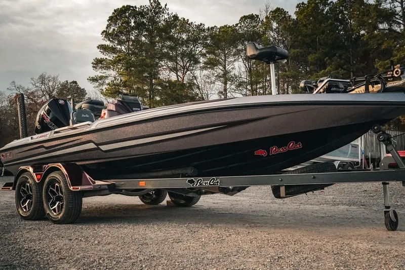 Slide: The Image of 2026 Bass Cat Lynx STS boat on trailer, parked outdoors with trees in background. - 3