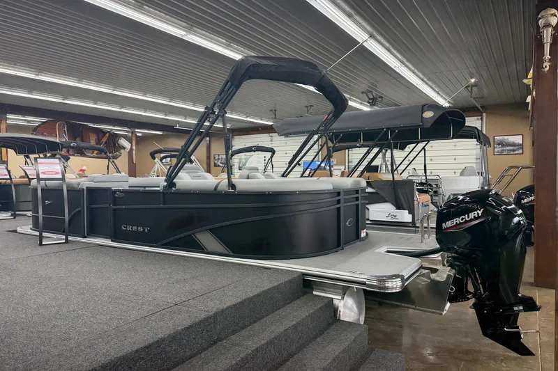Slide: The Image of 2026 Crest Conquest 215 SLC pontoon boat displayed indoors with Mercury engine. - 12