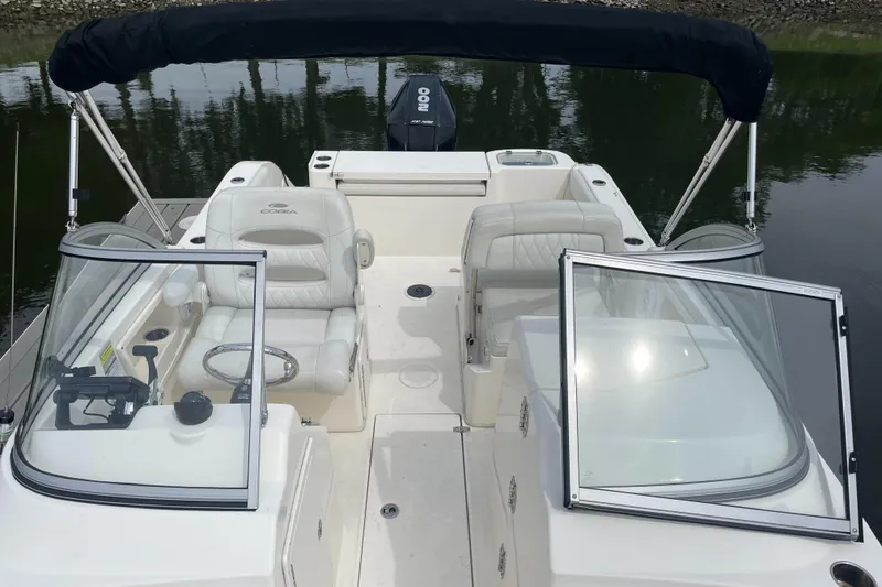 Slide: The Image of 2021 Cobia 220 Dual Console boat with open seating and black canopy on calm water. - 3