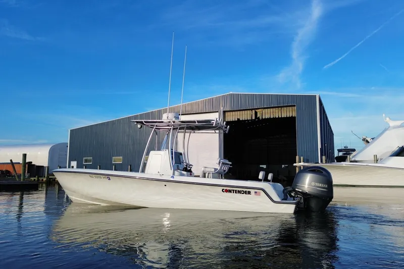 Slide: The Image of 2023 Contender 24 Sport boat docked near a large warehouse, clear blue sky. - 10