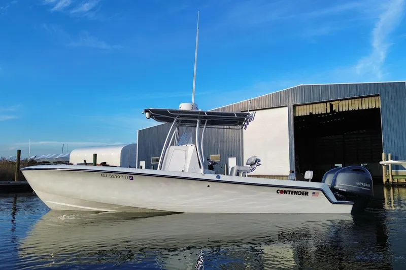 Slide: The Image of 2023 Contender 24 Sport boat docked near a large warehouse, under a clear blue sky. - 11