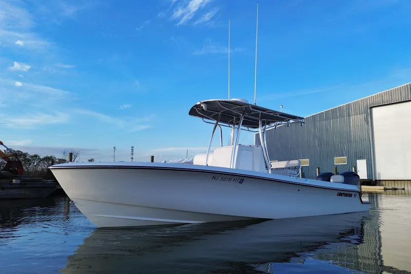 Slide: The Image of 2023 Contender 24 Sport boat docked by a warehouse under a clear blue sky. - 12