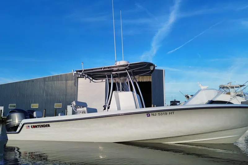 Slide: The Image of 2023 Contender 24 Sport boat docked near a marina under a clear blue sky. - 15