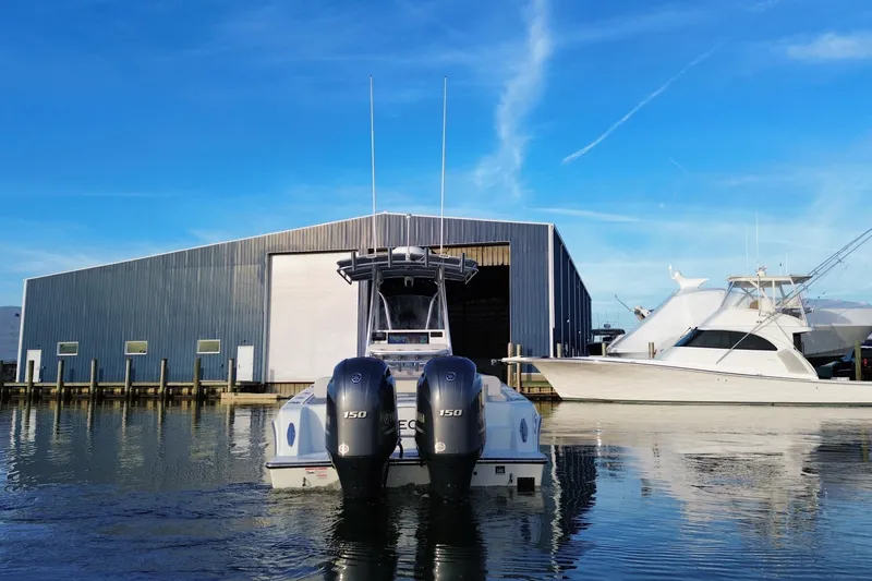 Slide: The Image of 2023 Contender 24 Sport boat docked near a large warehouse, clear blue sky. - 7
