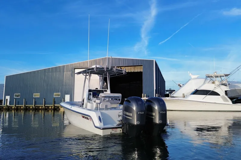 Slide: The Image of 2023 Contender 24 Sport boat docked near a large warehouse, clear blue sky. - 8