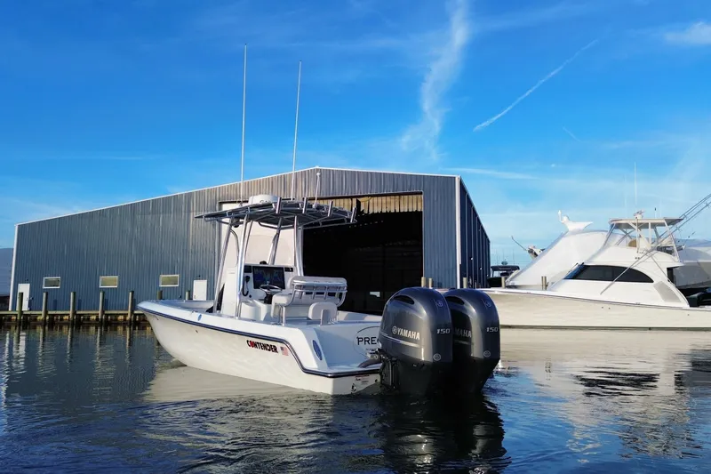 Slide: The Image of 2023 Contender 24 Sport boat docked with dual Yamaha engines, near a marina. - 9