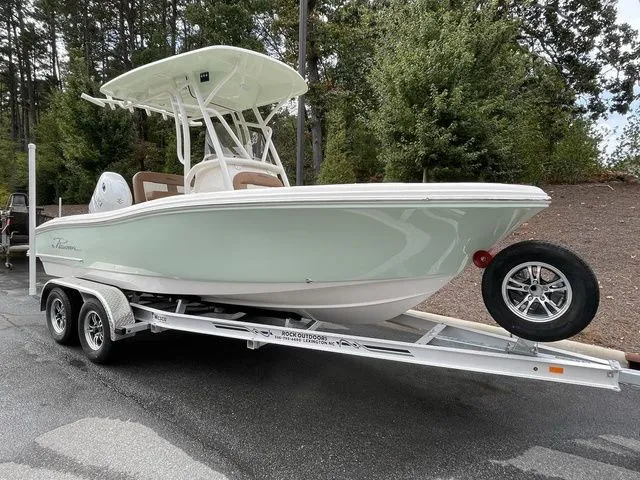 Slide: The Image of 2024 Pioneer Sportfish 202 boat on trailer, parked outdoors, surrounded by trees. - 2