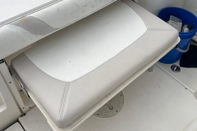 Slide: The Image of 2006 Boston Whaler 240 Outrage boat seat with white upholstery and nearby blue bucket. - 12