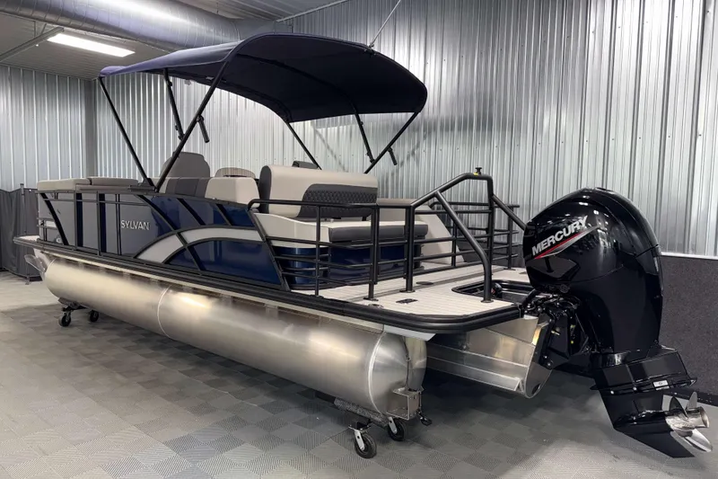 Slide: The Image of 2026 Sylvan L3 CLZ DH pontoon boat with Mercury outboard motor in a metal-walled showroom. - 24
