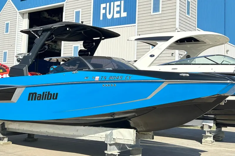 Slide: The Image of 2019 Malibu Wakesetter 24 MXZ boat in vibrant blue, docked near a fuel station. - 8