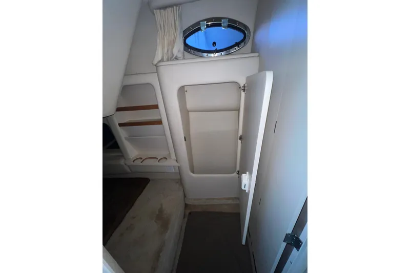Slide: The Image of 1999 Sea Ray 290 Sundancer cabin interior with open storage compartment and porthole window. - 28