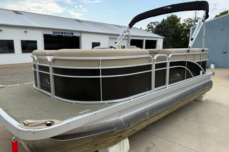 Slide: The Image of 2015 Bennington 18 SLX pontoon boat outside showroom, featuring beige seating and black paneling. - 8