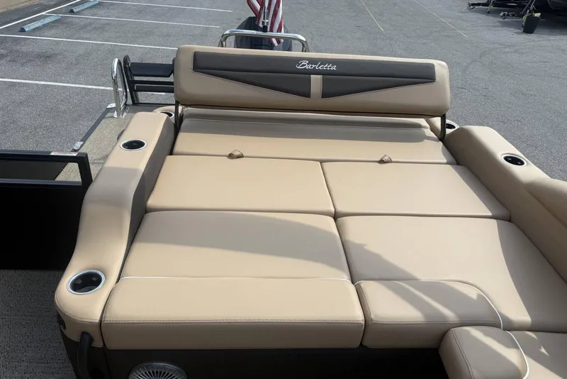 Slide: The Image of 2025 Barletta Cabrio 24U boat with beige seating and cup holders, parked on asphalt. - 21