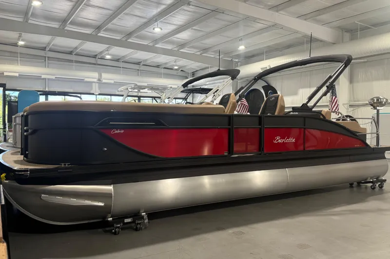 Slide: The Image of 2026 Barletta Cabrio 24UC pontoon boat in showroom, featuring sleek red and black design. - 2