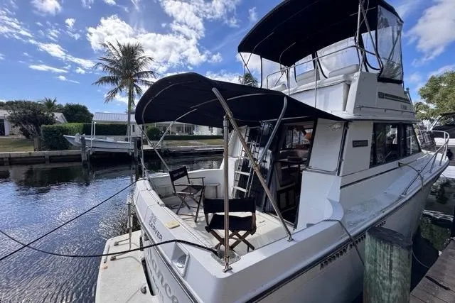 Slide: The Image of 1987 Carver 32 Aft Cabin Motor Yacht docked by a palm tree under a blue sky. - 7