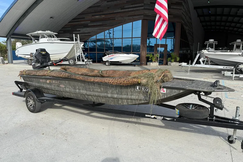 Slide: The Image of 2026 War Eagle 750 Gladiator boat on trailer, parked outside a modern building. - 2