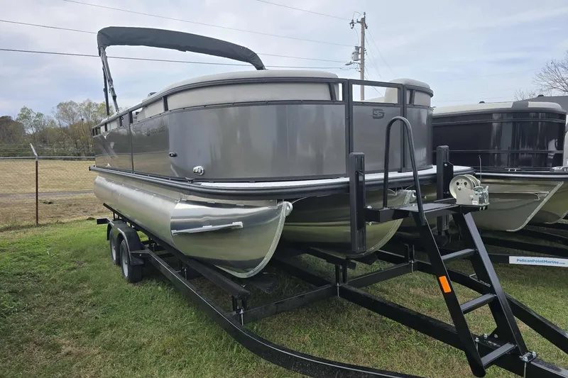 Slide: The Image of 2026 Dockside pontoon boat on trailer, parked on grass, with overcast sky. - 2