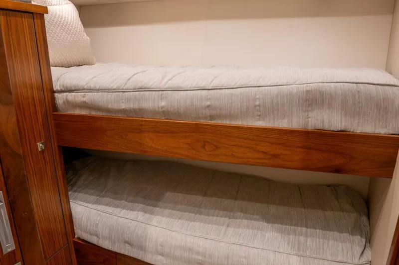 Slide: The Image of Bunk beds in 2018 Viking 80 Enclosed Bridge yacht cabin, featuring wooden accents and cozy bedding. - 23