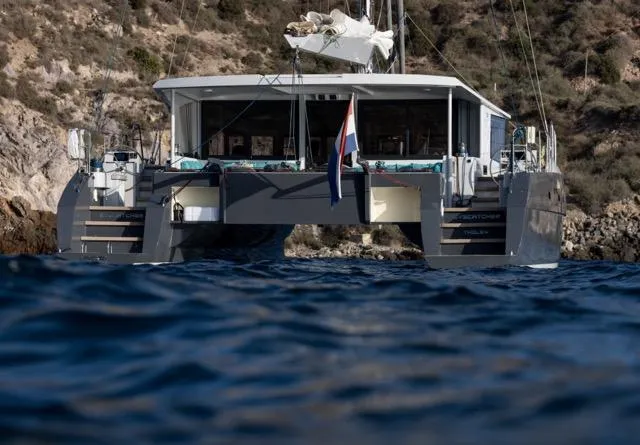 Slide: The Image of Catamaran Eyecat 55 Autumn 2024 on water, with scenic rocky coastline backdrop. - 9