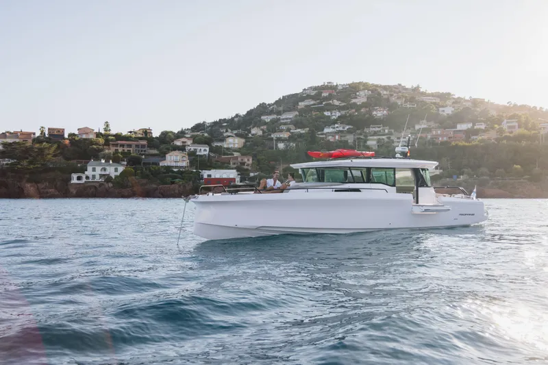 Slide: The Image of 2026 Axopar 45 XC AC Sandstone Lithium cruising near scenic coastal homes. - 1