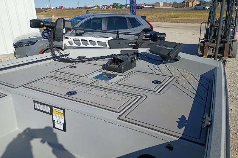 Slide: The Image of 2025 Avid 20 Rogue SC boat deck with fishing equipment and parked cars in the background. - 2