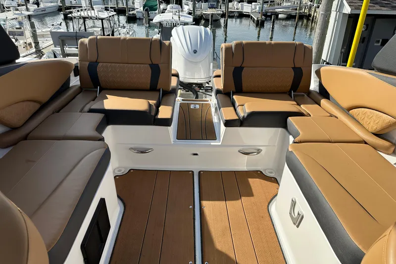 Slide: The Image of 2024 Hurricane SunDeck 2600 OB boat interior with tan seating and wood flooring at marina. - 8