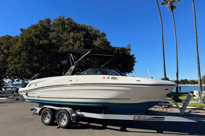 Slide: The Image of 2022 Bayliner VR6 Bowrider OB on trailer, parked near a lake with palm trees. - 7