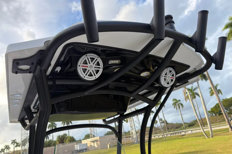 Slide: The Image of 2019 Wellcraft 241 Bay boat T-top with speakers and rod holders, set against a tropical backdrop. - 19