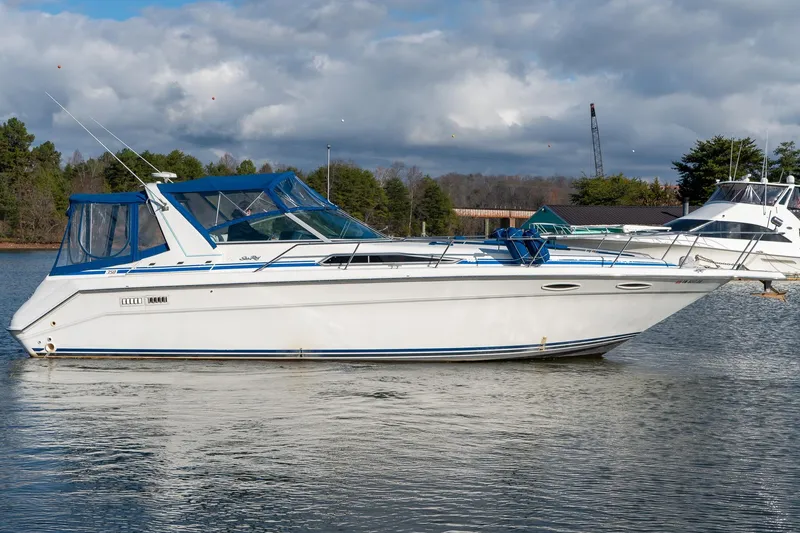 Slide: The Image of 1991 Sea Ray 350 Sundancer boat on calm water, blue canopy, scenic background. - 5