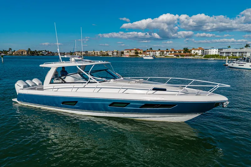 Slide: The Image of 2024 Intrepid 477 Evolution yacht cruising on a sunny day with coastal buildings in the background. - 2