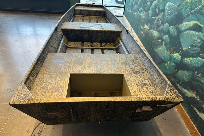 Slide: The Image of 2026 Tracker Grizzly 15 Jon boat with camouflage pattern, displayed indoors. - 2