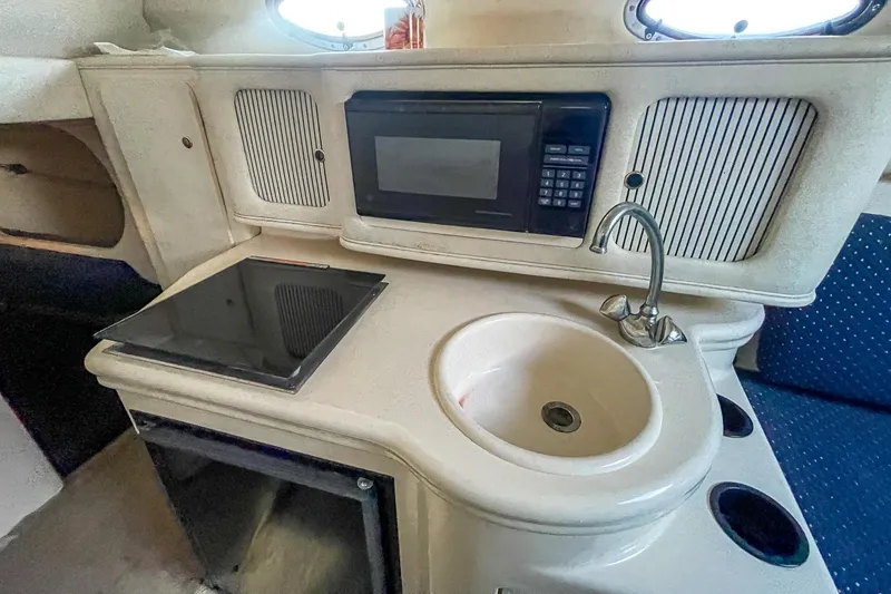 Slide: The Image of 2000 Sea Ray 260 Sundancer interior with sink, stove, and microwave in compact kitchen area. - 23