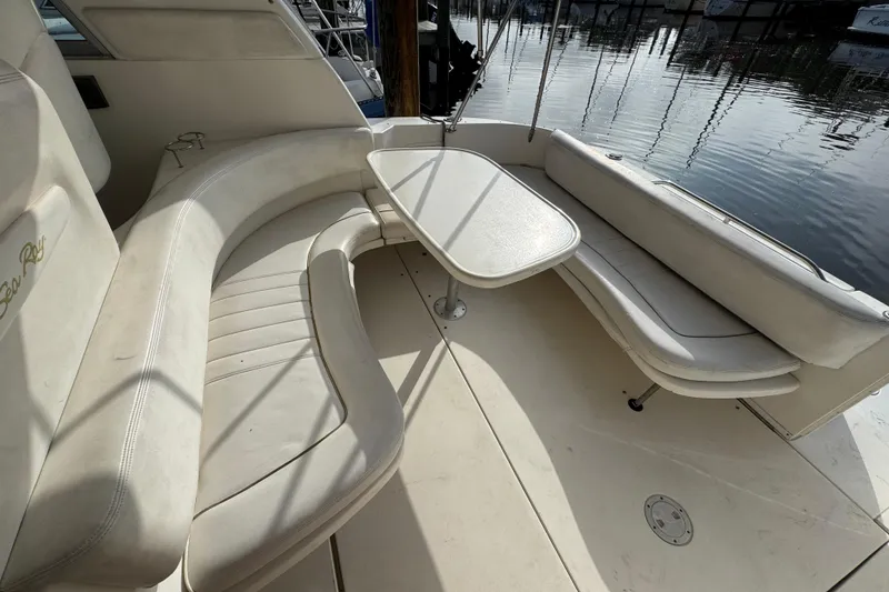 Slide: The Image of 2002 Sea Ray 310 Sundancer boat interior with curved seating and table by the water. - 5