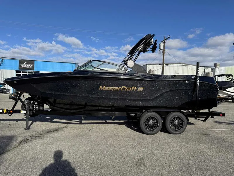 The Image of 2025 MasterCraft XT24 boat on trailer, black exterior, parked outdoors. - 1
