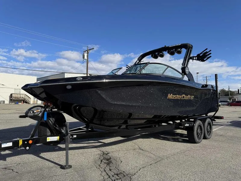 Slide: The Image of 2025 MasterCraft XT24 boat on trailer, black exterior, parked outdoors. - 2