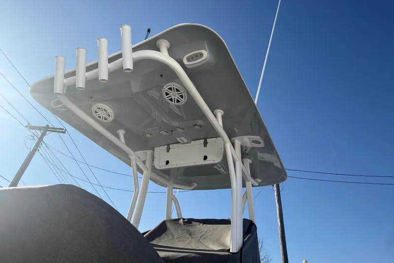 Slide: The Image of 2026 Sea Hunt Ultra 229 boat T-top with rod holders and speakers under clear blue sky. - 8