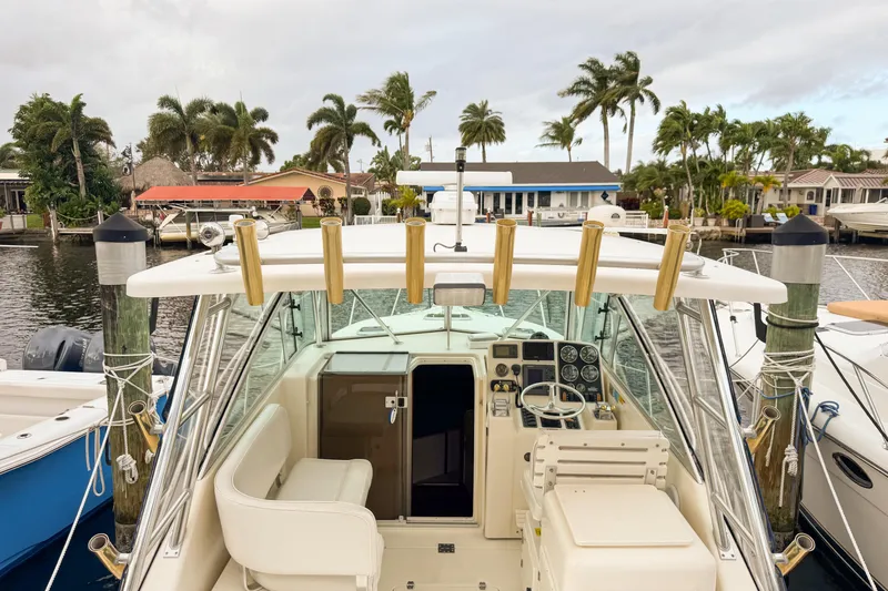 Slide: The Image of 2002 Pursuit 3000 Express boat docked, featuring helm and seating area, with palm trees in background. - 105