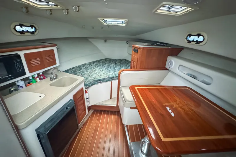 Slide: The Image of 2002 Pursuit 3000 Express cabin interior with kitchenette, bed, and wooden table. - 43