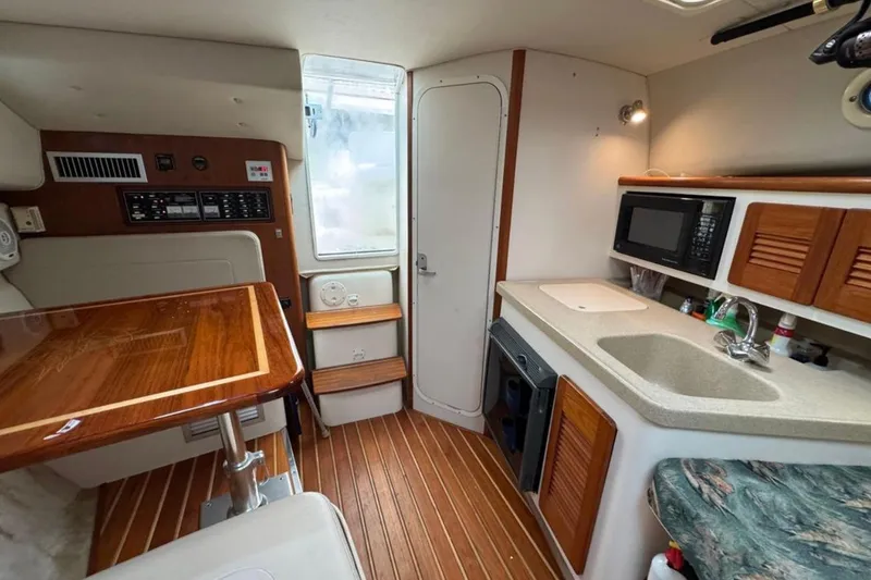 Slide: The Image of 2002 Pursuit 3000 Express cabin interior with kitchenette, wooden table, and seating area. - 50