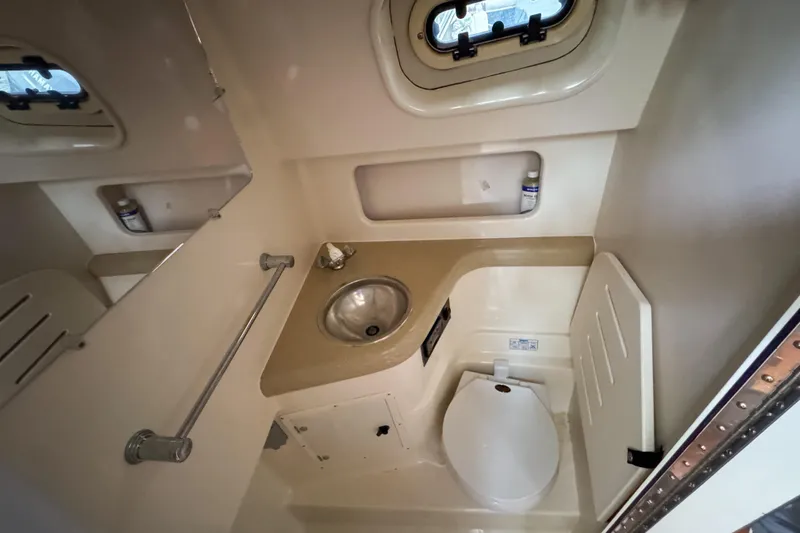 Slide: The Image of 2002 Pursuit 3000 Express boat bathroom with sink, toilet, and porthole window. - 66