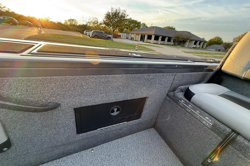 Slide: The Image of 2018 Tracker Targa 18 WT interior with storage compartment, set against a grassy landscape. - 63