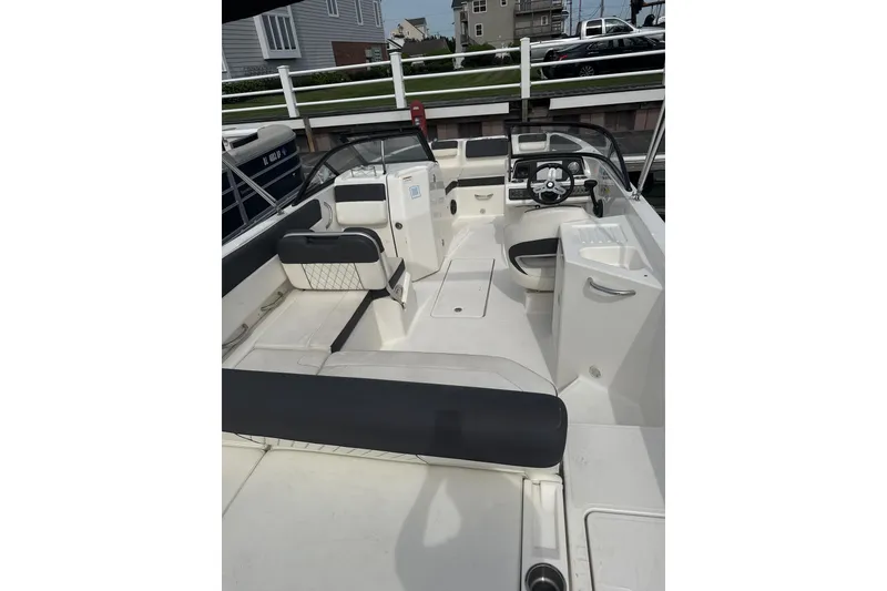 Slide: The Image of 2023 Bayliner DX 2200 boat interior with seating and steering wheel, docked near houses. - 6