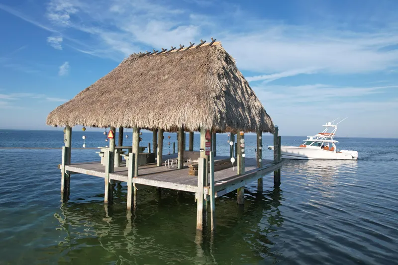 Slide: The Image of Thatch-roofed dock with 2019 Scout 420 LXF boat on calm ocean waters. - 10